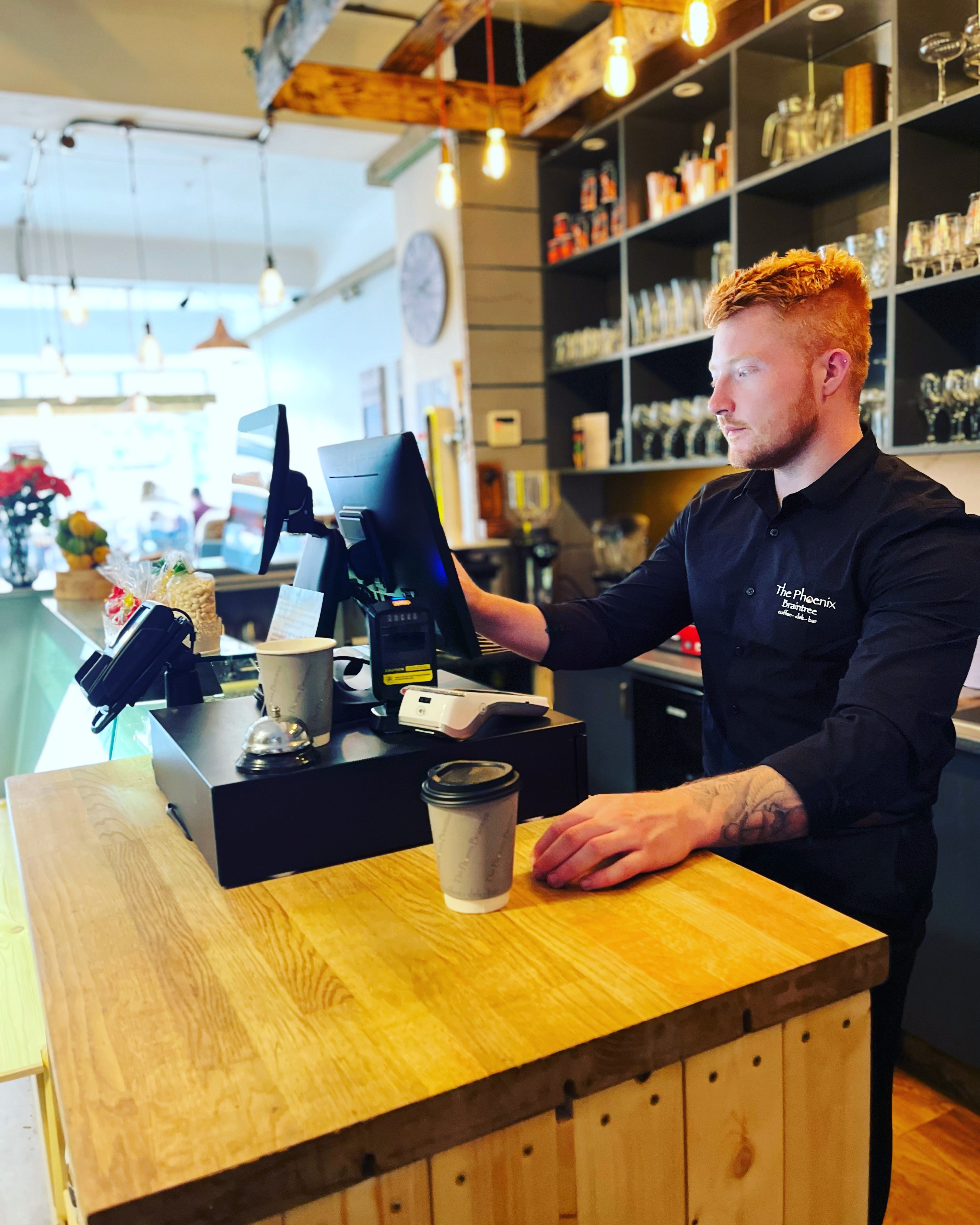 Manager stands at till in new deli bar wearing black shirt